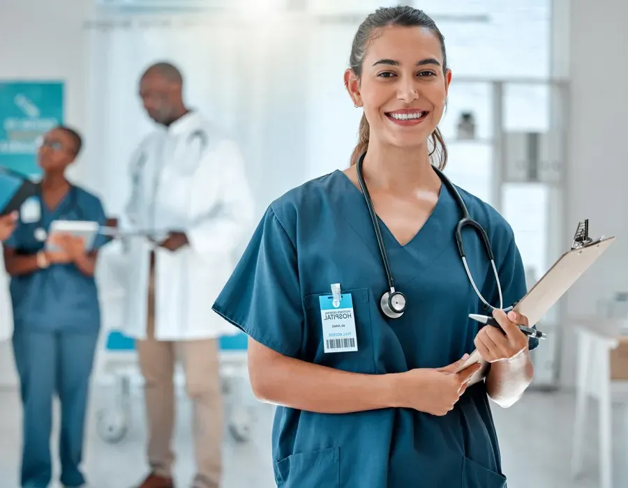 Medical assistant wearing green scrubs smiling with clipboard